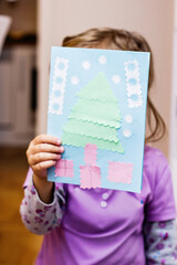Child holding a handmade Christmas card with tree and gifts