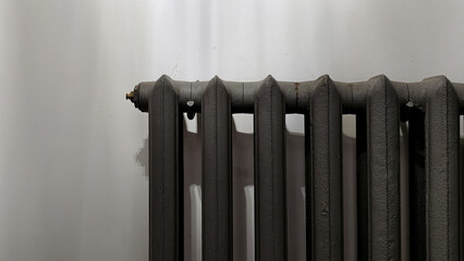 A vintage industrial element: an antique black cast-iron radiator against a clean white wall. Small...