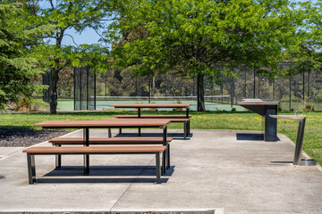 Public park picnic area with picnic tables and outdoor drinking fountains beside a tennis court in suburban Australia. Concept of community amenity, public outdoor facilities,recreation infrastructure