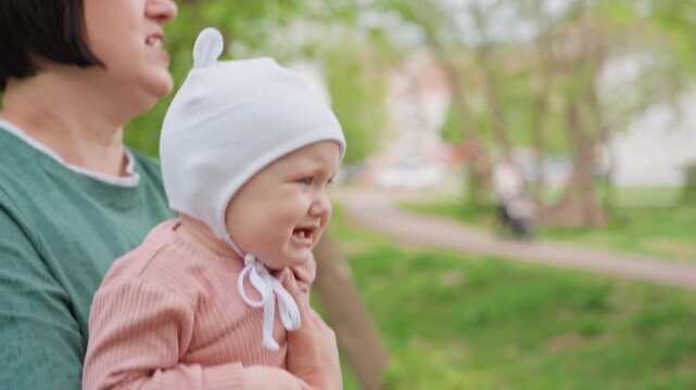 Child Cries Outdoors, Infant Exhibits Distress While Held By Caregiver In Park Setting, Distressed Infant Expresses Discomfort In Caregiver Arms Amidst Park Greenery With Family Close By