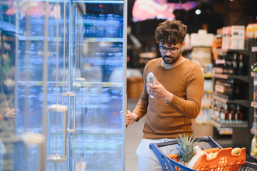 Arab customer choosing bottled water in supermarket refrigerator section