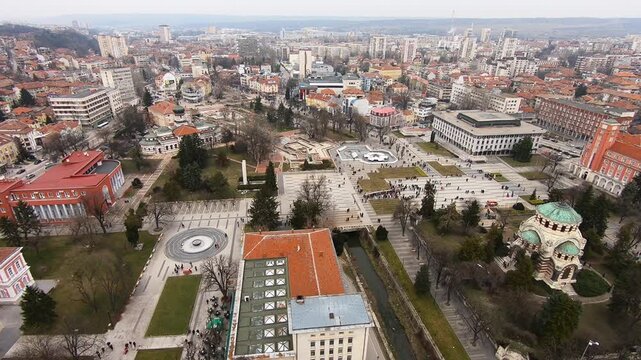 Drone video of Pleven center on March 3, 2019, showing landmarks, the square, the Ossuary, church, municipal building, fountains, and people walking with a long national flag, Pleven, BG,03 March 2019