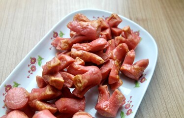 A generous portion of savory pink sausages, cut into flower or octopus shapes, is served on a patterned white platter against a simple wooden table background.