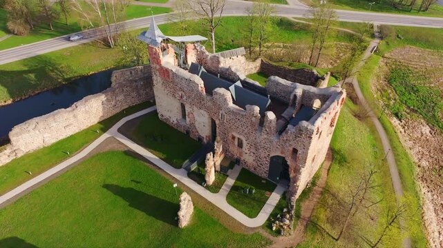 Ancient stone walls of Dobele Castle glow in warm sunlight and spring grass