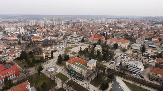 Drone video of Pleven center on March 3, 2019, showing landmarks, the square, the Ossuary, church, municipal building, fountains, and people walking with a long national flag, Pleven, BG,03 March 2019