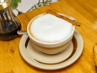 Close up, Hot cappuccino in a white cup with cinnamon bark on a wooden table.