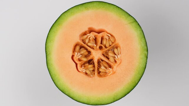 Rotating half green netted melon close-up. Fresh cantaloupe showing orange flesh and seeds. Healthy food concept.
