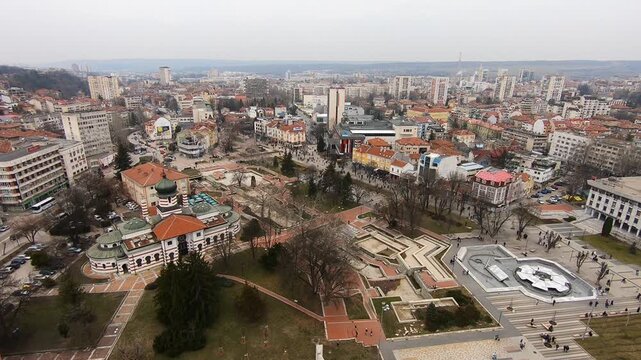 Drone video of Pleven center on March 3, 2019, showing landmarks, the square, the Ossuary, church, municipal building, fountains, and people walking with a long national flag, Pleven, BG,03 March 2019