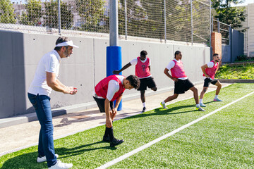 Soccer team performing dynamic stretching exercises on artificial turf with coach supervising during a training session
