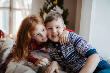 Small girl and boy in pajamas indoors at home at Christmas, playing.