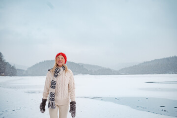 Senior woman enjoying snowfall in winter landscape.