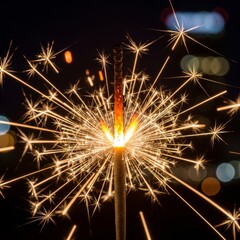 Obraz premium Macro detail of a burning sparkler ejecting gold sparks against a dark night background.