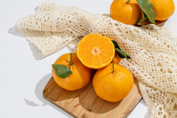 Fresh ripe tangerines and a glass of orange juice on white table with sunlight and shadows