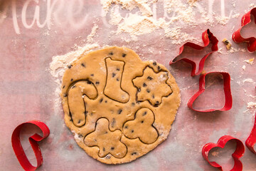 Homemade Christmas cookie preparation with dough, flour, cookie cutters and festive decorations on a kitchen table. Holiday baking process with ingredients and gingerbread shapes.
