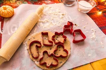Homemade Christmas cookie preparation with dough, flour, cookie cutters and festive decorations on a kitchen table. Holiday baking process with ingredients and gingerbread shapes.