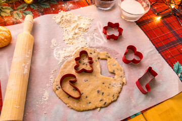 Homemade Christmas cookie preparation with dough, flour, cookie cutters and festive decorations on a kitchen table. Holiday baking process with ingredients and gingerbread shapes.
