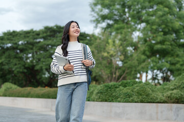 Young asian woman student walking with laptop on campus