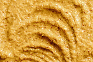 Mustard sauce with grains close-up. Hot spices as a background. Texture of Dijon mustard.
