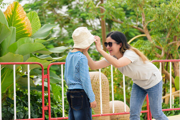 Mother woman child son family parent enjoy summer city street activity people outdoors, loving parent gently adjusts boy bucket hat, happy joyful interaction with vibrant under bright sky