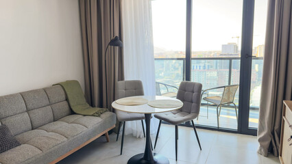 Modern cozy living room with soft neutral tones, round dining table and panoramic balcony view