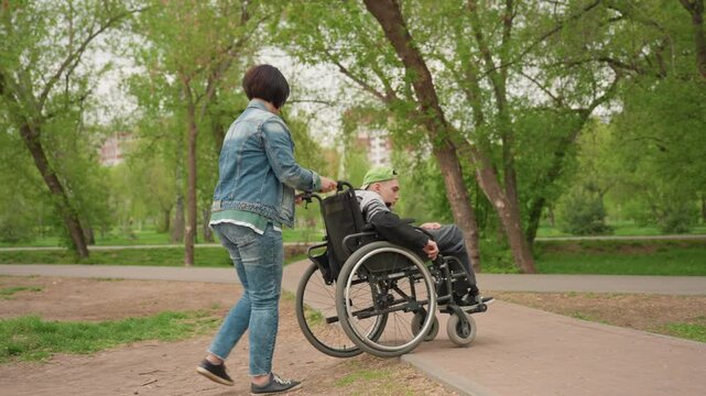 Gentle Woman Guides Wheelchair Along Scenic Trail, Peaceful Park Walk As Woman Assists With Caring Attention, Serene Stroll Through Leafy Park While Woman Lovingly Supports Wheelchair User