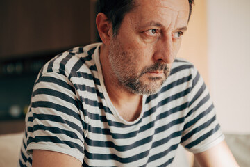 Obraz premium Thoughtful tired middle-aged man in striped shirt staring away, showing stress, concern, and emotional fatigue.