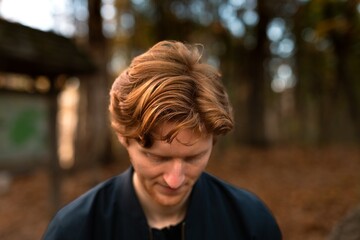 Young man with long, wavy hair looks down in a forest setting