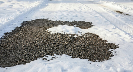 Patchy snow on gravel driveway, dark stones exposed on cold ground. Melting snow on gravel driveway creates rough texture of ice and stone. Snow on gravel driveway useful for winter background.