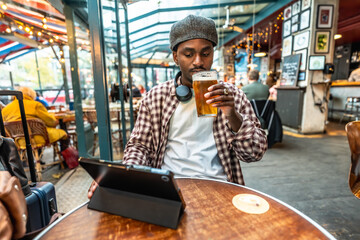 Young man enjoying beer and tablet in pub, traveling solo