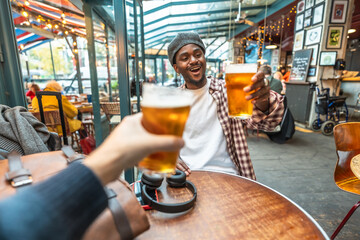 Young man toasting beer glasses with friend at pub