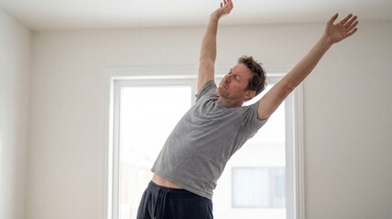 Relaxed middle-aged man doing morning stretches with arms raised in a bright, modern, minimalist apartment living room.