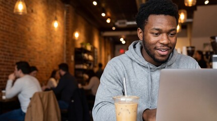 Young Black man smiling while working on his laptop computer in a cozy coffee shop with warm ambient lighting.