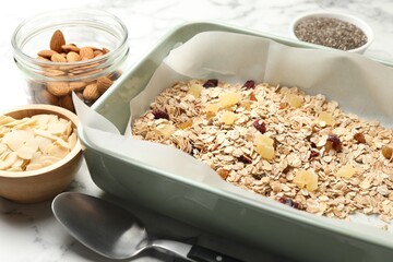 Making granola. Oat flakes, dried fruits, almond nuts and honey on white marble table, closeup