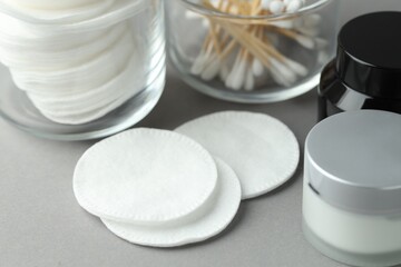 Clean cotton pads, swabs and cosmetic products on light grey background, closeup