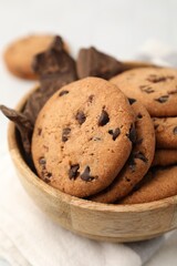 Yummy chocolate chip cookies and pieces of chocolate in bowl on white table, closeup