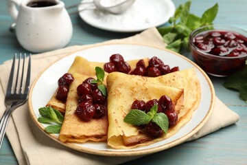 Delicious crepes served with cherry jam on light blue wooden table, closeup