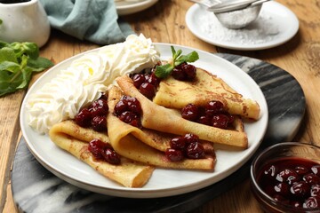 Tasty crepes with cherries, whipped cream and mint served on wooden table, closeup