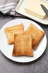 Fresh toasted bread slices served with butter on grey table, closeup