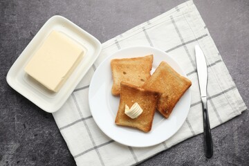 Fresh toasted bread slices with butter on grey table, flat lay