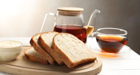 Bread slices with butter and tea on white wooden table, closeup