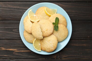 Tasty lemon cookies and fruit slices on black wooden table, top view
