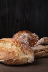 Different types of bread loaves on wooden table, closeup