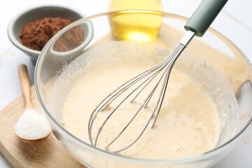 Different ingredients for dough and whisk on table, closeup