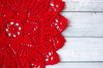 Red crocheted doily placed on a gray wooden background, creating a simple yet elegant handmade textile composition suitable for craft themes, rustic decor, and seasonal creative designs.
