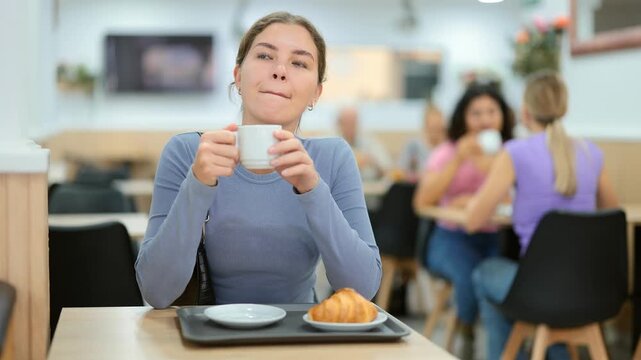 Attractive young female sitting alone at table in cozy cafe, drinking fragrant coffee . High quality 4k footage