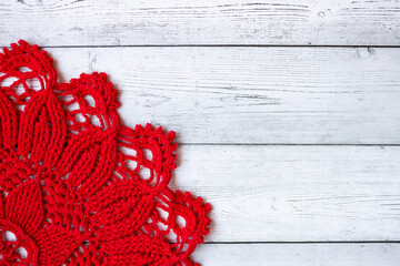 Red crocheted doily placed on a gray wooden background, creating a simple yet elegant handmade textile composition suitable for craft themes, rustic decor, and seasonal creative designs.