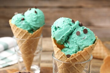 Tasty mint chocolate chip ice cream in waffle cones on wooden table, closeup