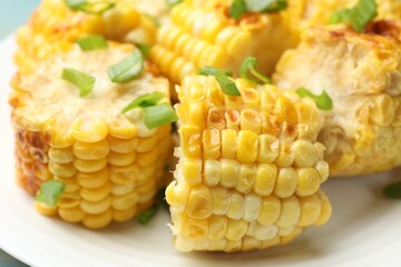 Pieces of grilled corn cobs with green onions on table, closeup