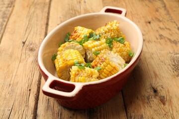 Pieces of grilled corn cobs with green onions on wooden table