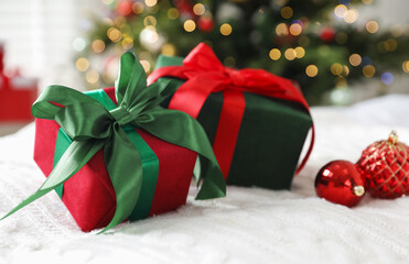 Gift boxes and Christmas baubles on bed against blurred lights indoors, closeup